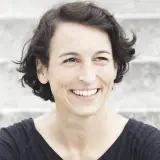 Lachende Frau mit kurzen Haaren, die an Madame Moneypenny Kritik erinnert.