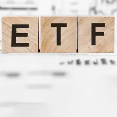 Holzwürfel mit den Buchstaben "ETF" stehen auf Finanzdokumenten. Ein ETF Sparplan ist eine einfache Möglichkeit, langfristig Vermögen aufzubauen.
