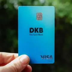 Eine blaue DKB Visa Debitkarte wird in der Hand gehalten, mit unscharfem Grün im Hintergrund.