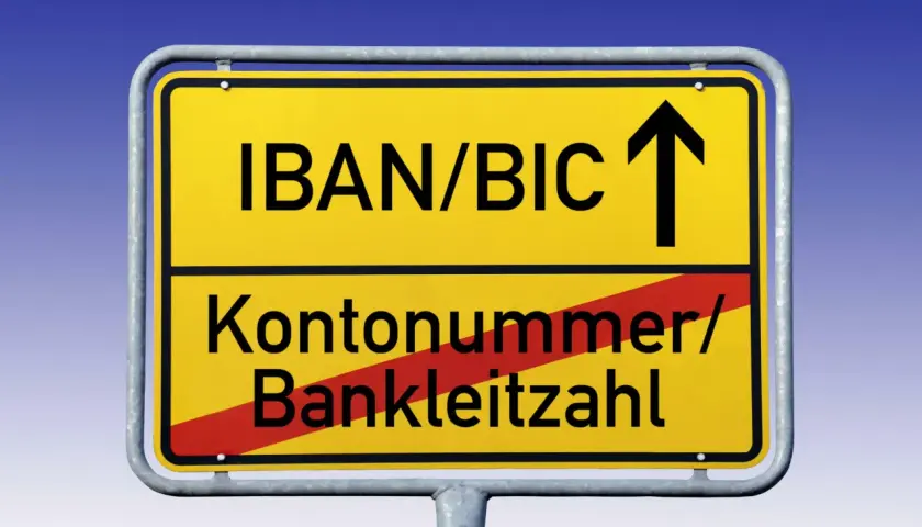 Gelbes Ortsschild mit "IBAN/BIC" und Pfeil nach oben. Darunter "Kontonummer/Bankleitzahl" durchgestrichen.