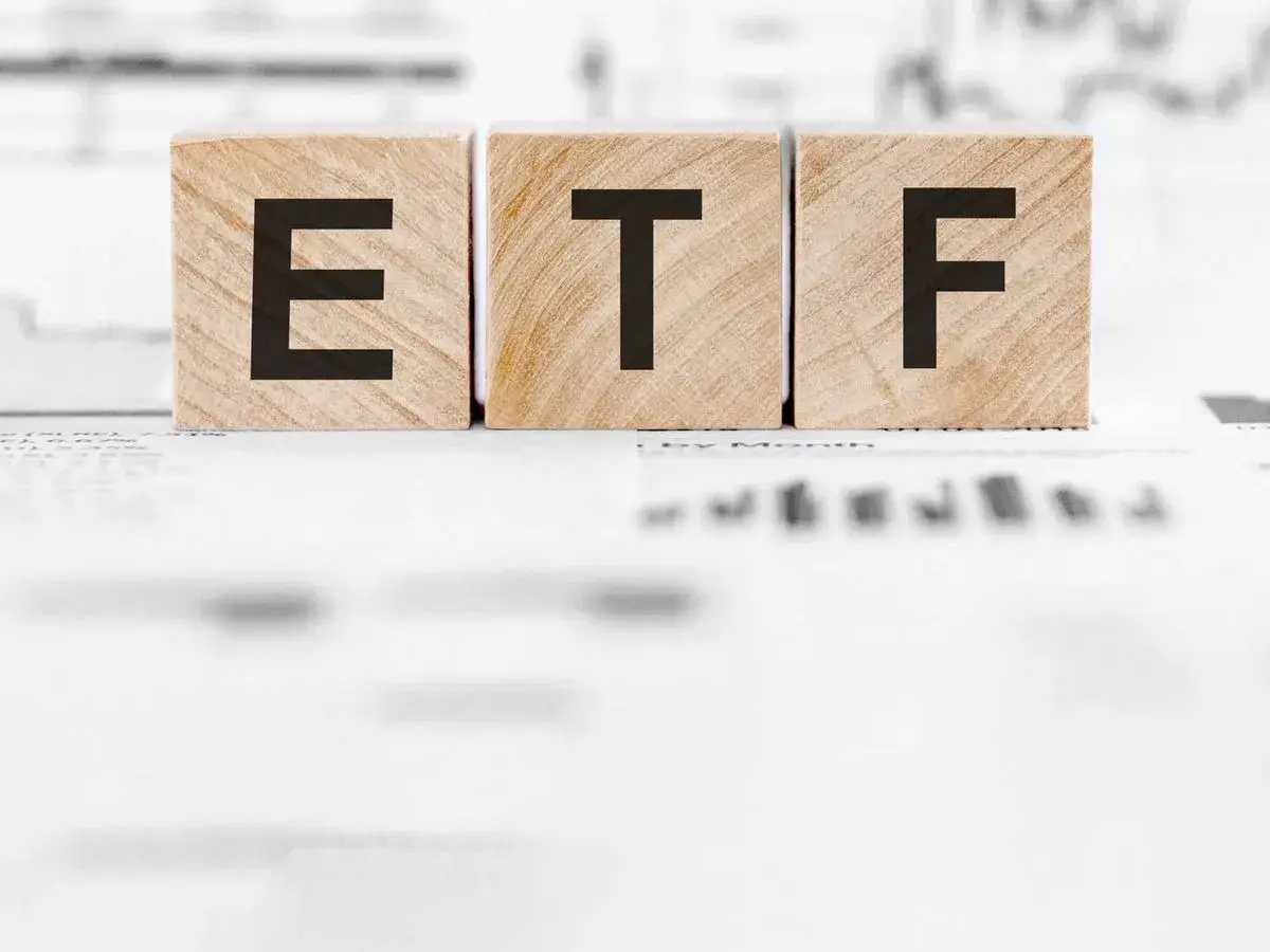 Holzwürfel mit den Buchstaben "ETF" stehen auf Finanzdokumenten. Ein ETF Sparplan ist eine einfache Möglichkeit, langfristig Vermögen aufzubauen.