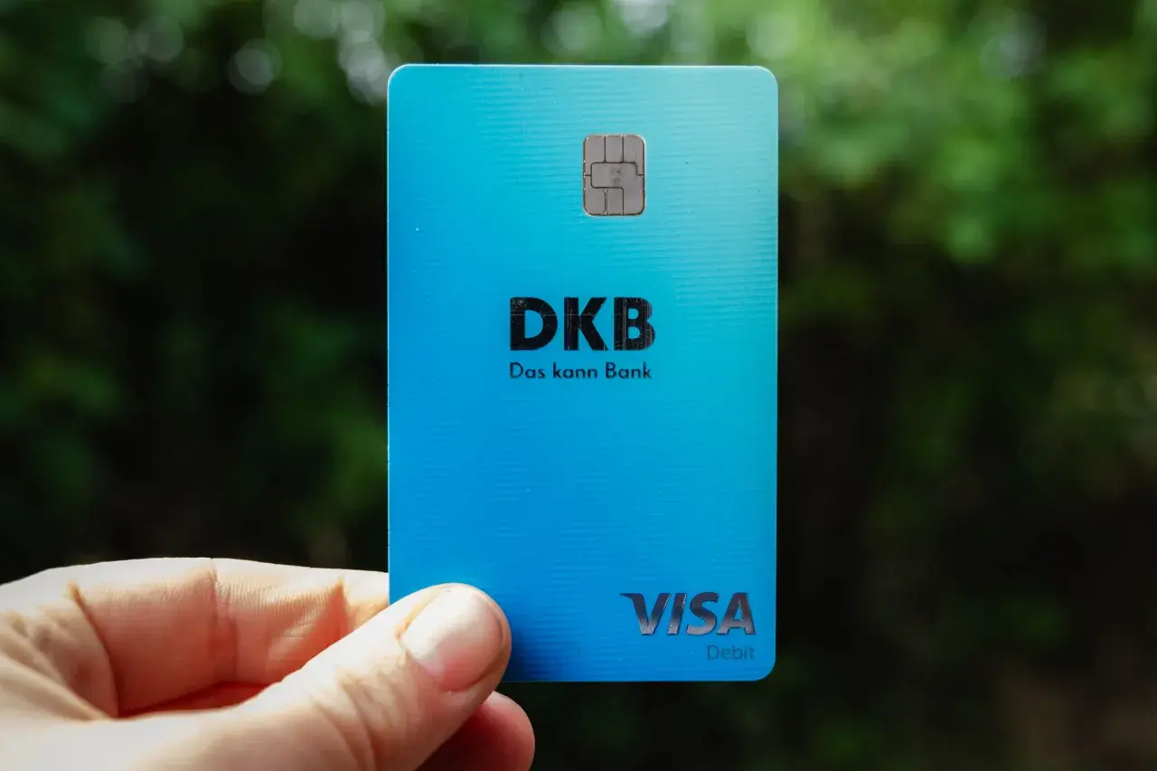 Eine blaue DKB Visa Debitkarte wird in der Hand gehalten, mit unscharfem Grün im Hintergrund.